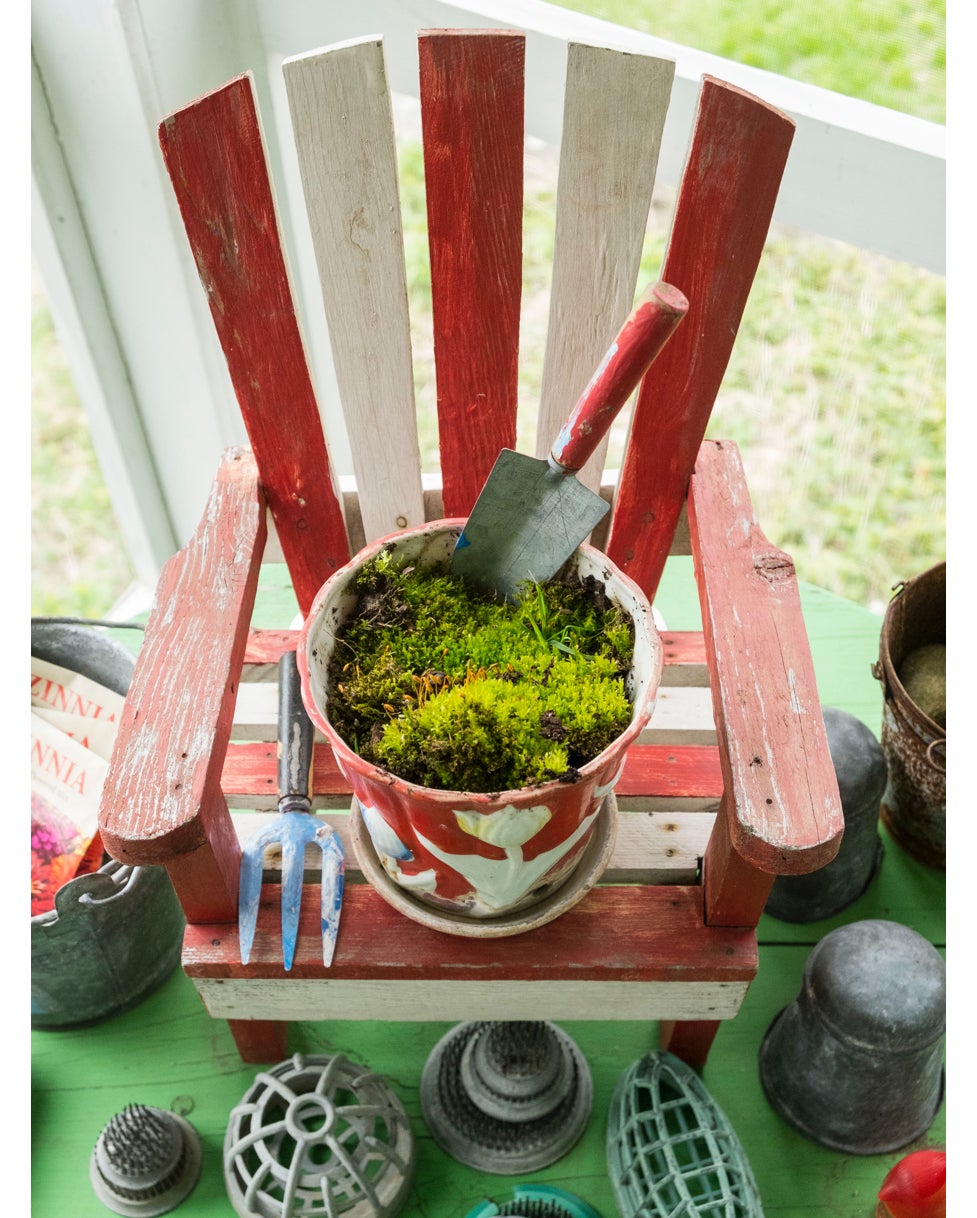 Un giardino segreto di muschio in un vaso da fiori vintage &egrave; sistemato su una piccola sedia Adirondack circondata da una collezione di flower frog