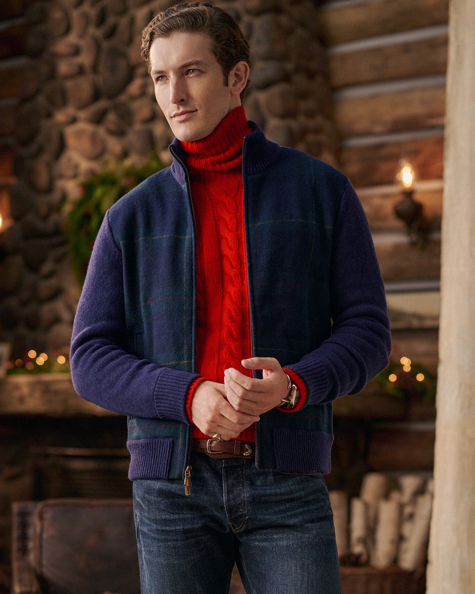 Uomo con una maglia dolcevita a trecce rossa, una giacca blu navy e jeans.